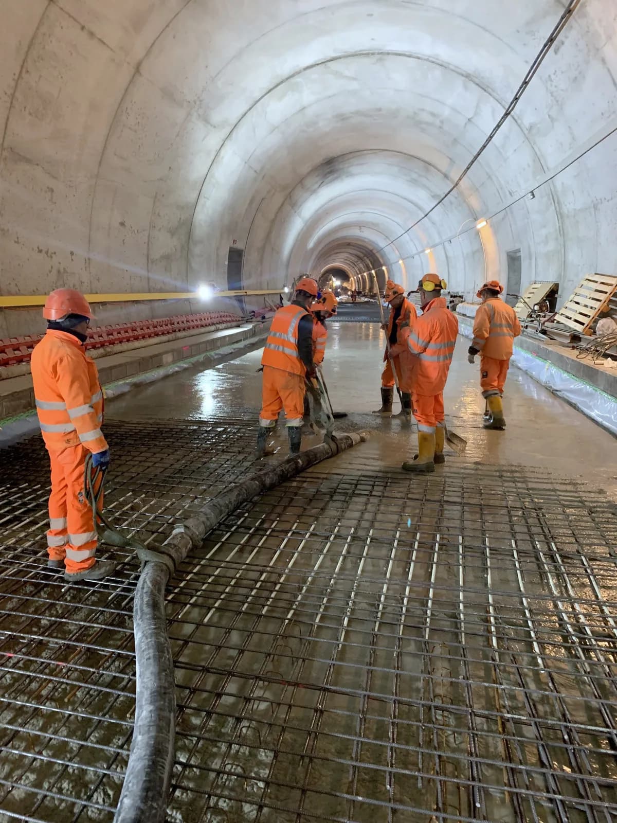 Team in oranger Arbeitskleidung beim Betonieren der Sohle eines Tunnels